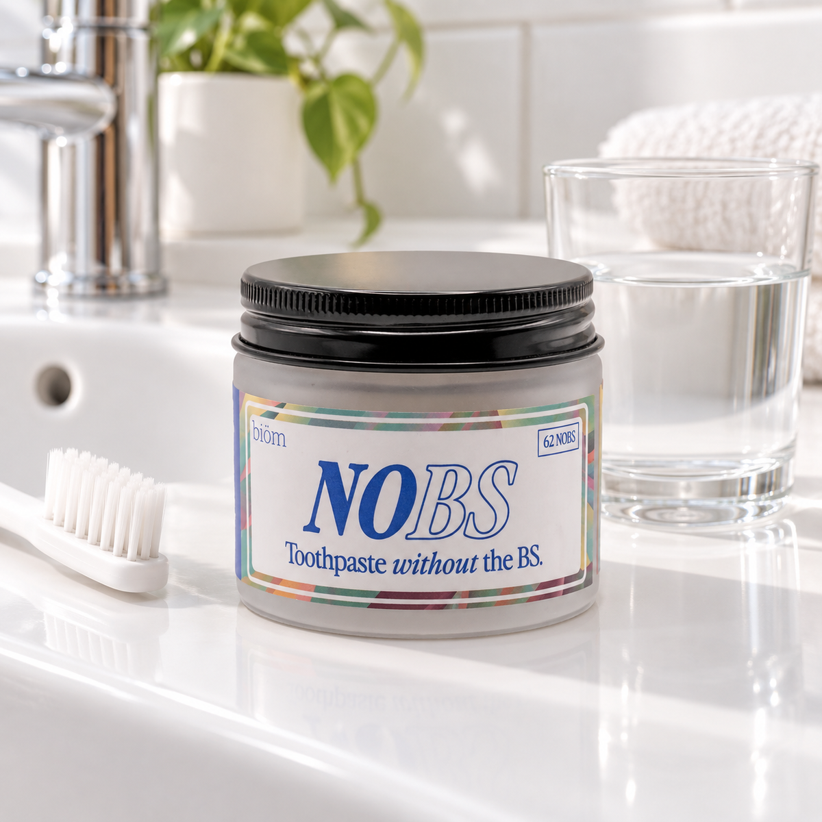 Illustrative bathroom scene with biöm NOBS 62 toothpaste tablets jar, toothbrush and glass of water